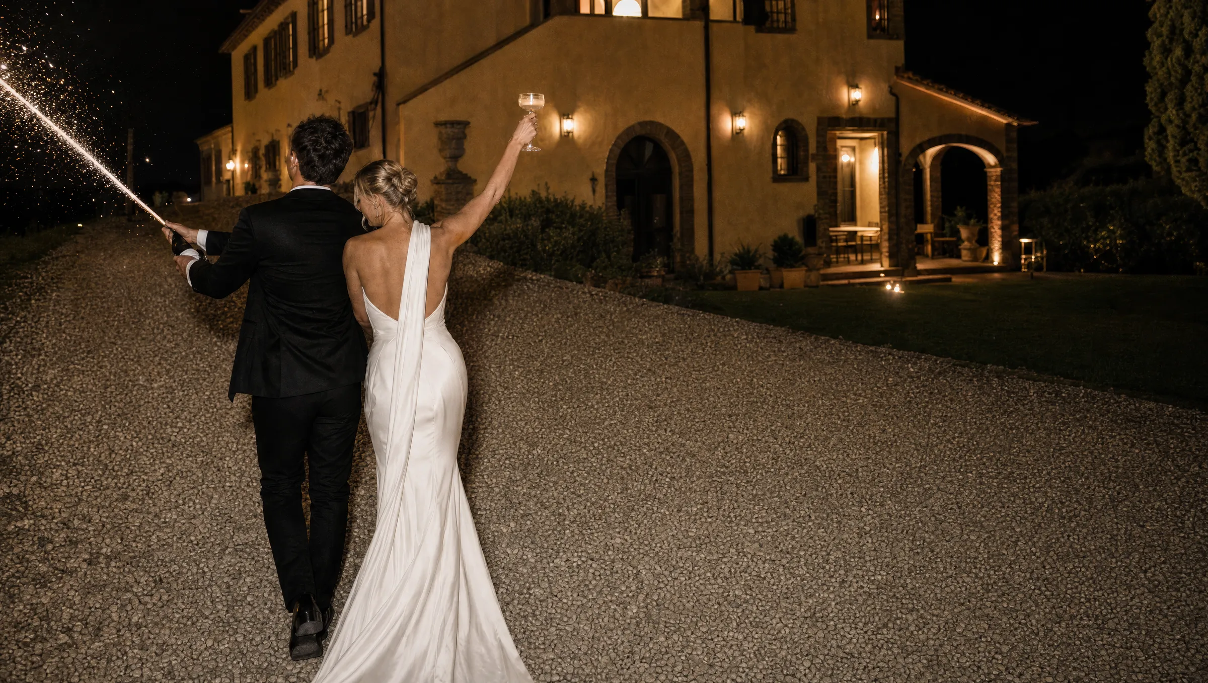 The newlyweds walk toward the lit villa at night, champagne raised and sparklers flying